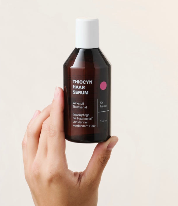 Eine linke Hand hält das Thiocyn Haarserum Frauen in der 150ml Flasche.