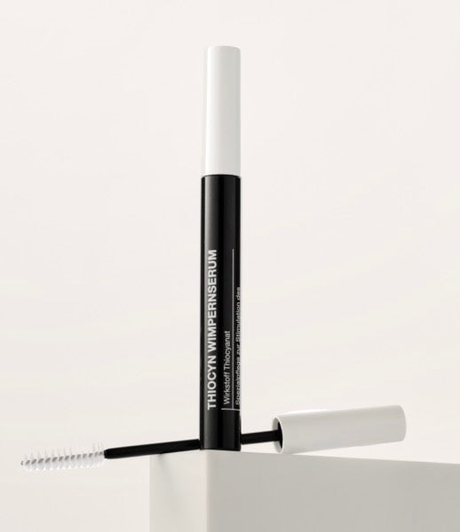 Das verschlossene Thiocyn Wimpernserum steht im Vordergrund, dahinter liegt die Wimpernbürste, mit der man das Serum aufträgt. Das verschlossene Thiocyn Wimpernserum steht im Vordergrund, dahinter liegt die Wimpernbürste, mit der man das Serum aufträgt.